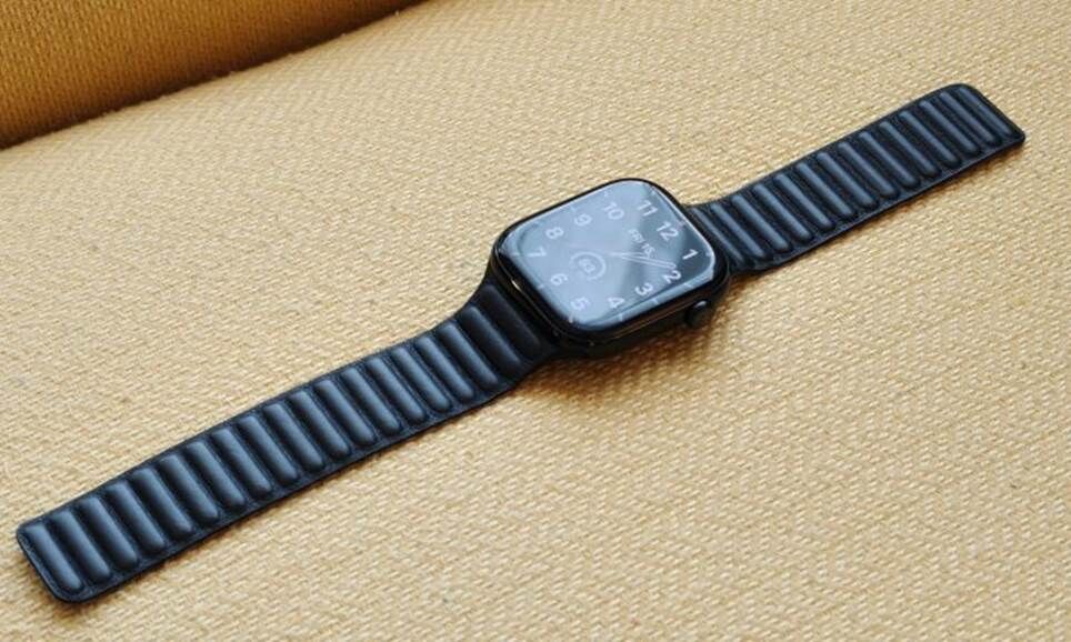 Chiếc Apple Watch Series 10 có dây đeo bằng da, nằm trên một chiếc ghế màu vàng.