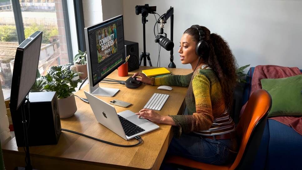 Một người phụ nữ đang ngồi ở bàn làm việc sử dụng MacBook Pro M5 được kết nối với một cặp màn hình.